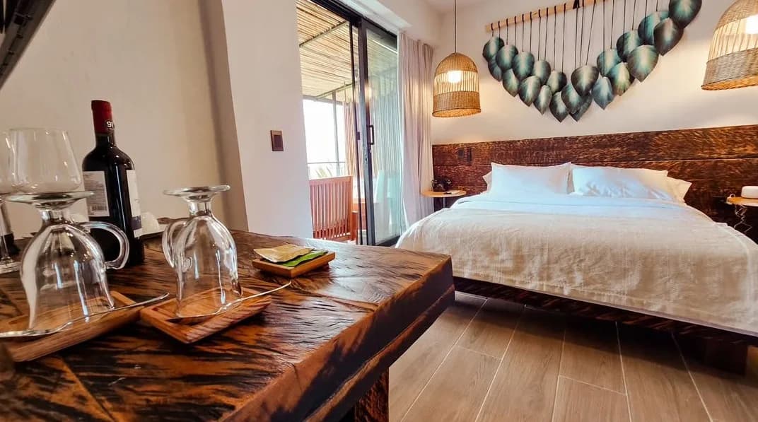 Habitación con cama doble, lámparas de mimbre y una botella de vino sobre la mesa de madera